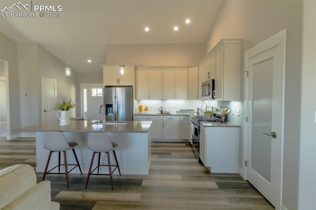 kitchen featuring decorative light fixtures, a center island with sink, white cabinets, and appliances with stainless steel finishes