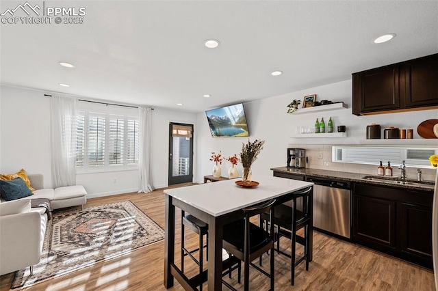 kitchen with sink, light hardwood / wood-style flooring, dark stone countertops, dark brown cabinetry, and stainless steel dishwasher