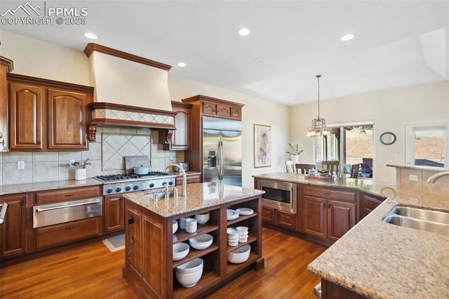 kitchen featuring sink, built in appliances, a center island with sink, dark hardwood / wood-style floors, and pendant lighting