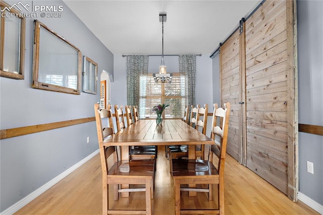 dining space with a barn door, a chandelier, and light hardwood / wood-style floors