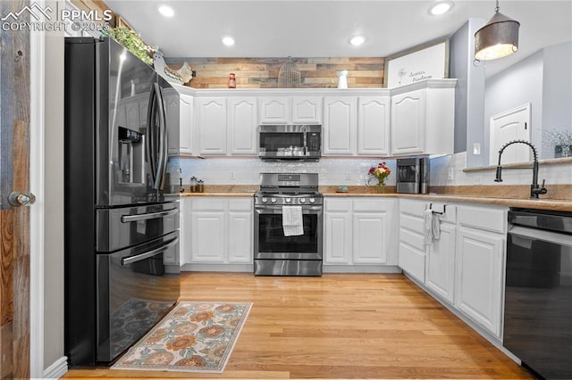 kitchen featuring appliances with stainless steel finishes, white cabinetry, hanging light fixtures, backsplash, and light wood-type flooring