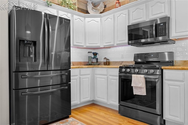 kitchen with backsplash, light hardwood / wood-style flooring, white cabinets, and appliances with stainless steel finishes