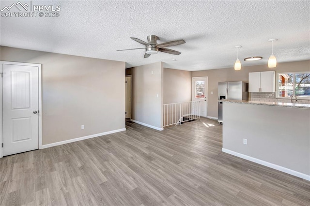 unfurnished living room with a textured ceiling, ceiling fan, and light hardwood / wood-style flooring