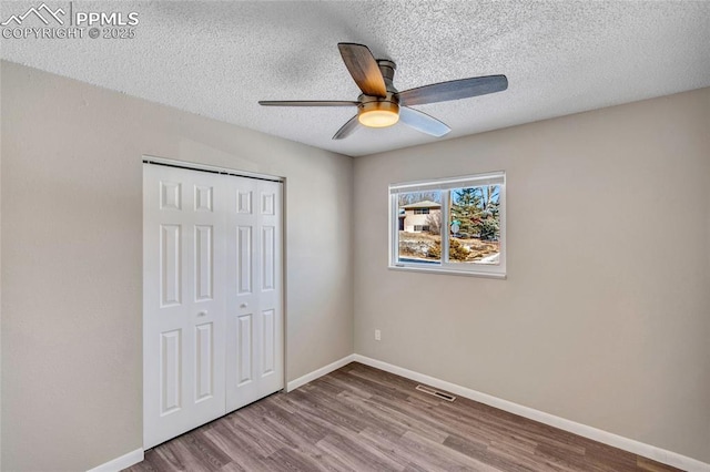 unfurnished bedroom with ceiling fan, a closet, a textured ceiling, and light wood-type flooring