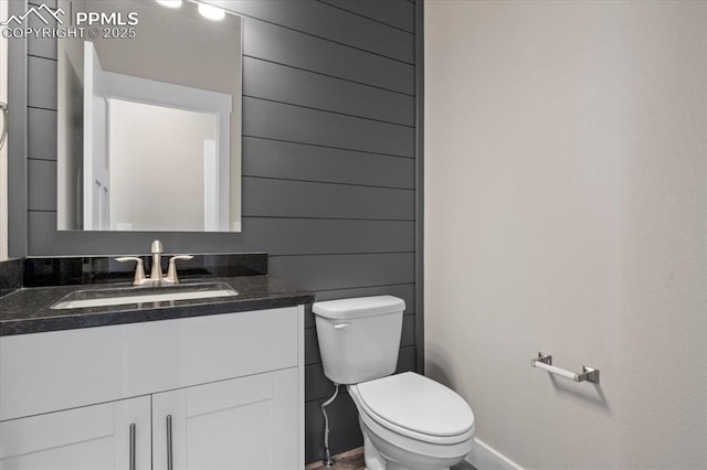 bathroom with vanity, toilet, and wood walls