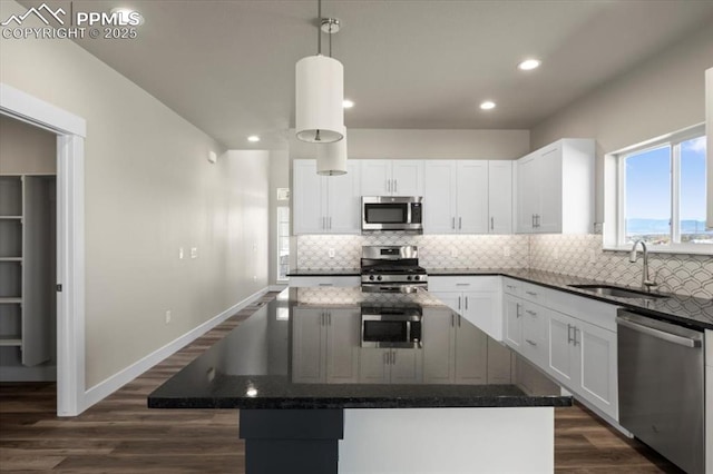 kitchen with sink, appliances with stainless steel finishes, white cabinets, a kitchen island, and decorative light fixtures