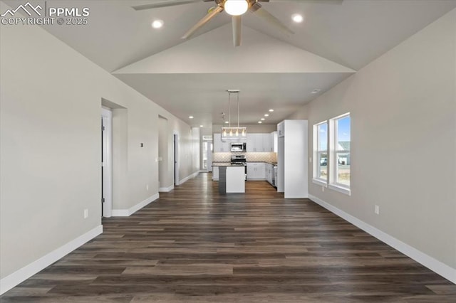 unfurnished living room featuring ceiling fan with notable chandelier, dark hardwood / wood-style floors, and vaulted ceiling