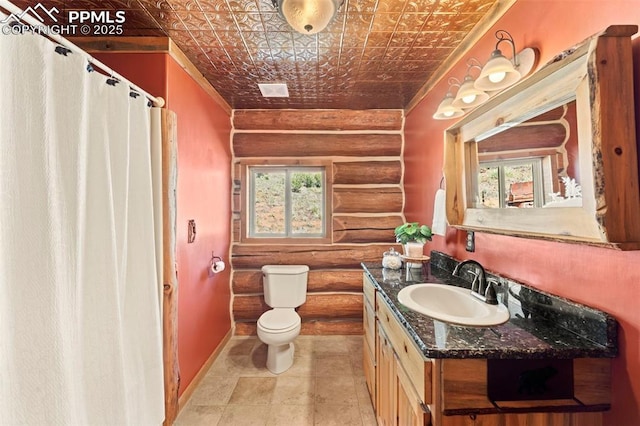 bathroom featuring a healthy amount of sunlight, toilet, rustic walls, and vanity