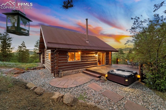 back house at dusk with a hot tub and a deck