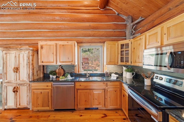 kitchen featuring sink, dark stone countertops, stainless steel appliances, light brown cabinetry, and log walls