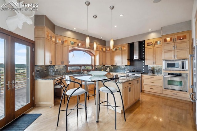 kitchen featuring dark stone countertops, wall chimney exhaust hood, stainless steel appliances, a center island with sink, and french doors