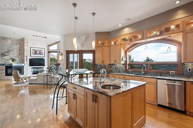 kitchen featuring dishwasher, sink, a center island with sink, and stone counters