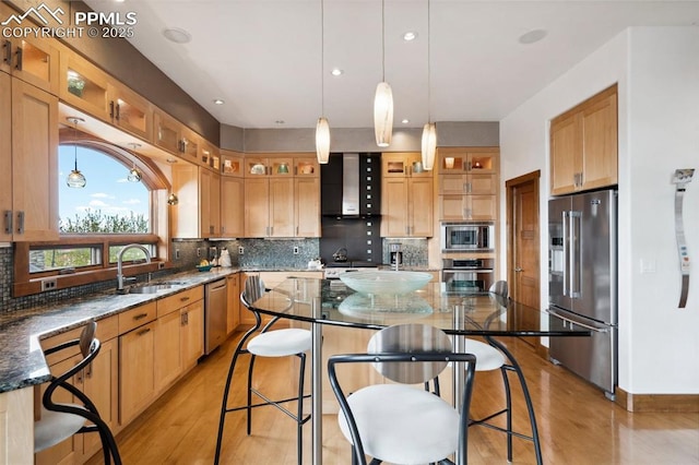 kitchen featuring wall chimney exhaust hood, dark stone countertops, appliances with stainless steel finishes, a kitchen island, and decorative backsplash