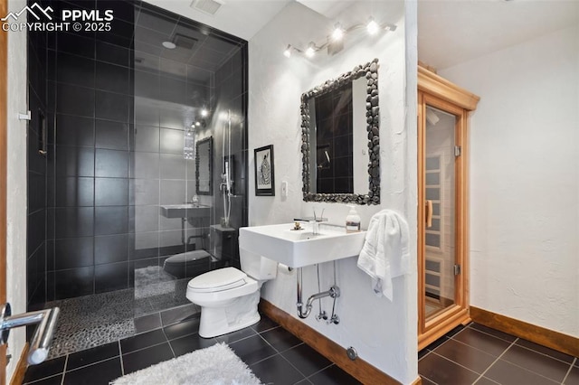 bathroom featuring tiled shower, toilet, and tile patterned flooring