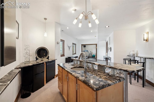 kitchen featuring sink, an island with sink, decorative light fixtures, light colored carpet, and dark stone counters