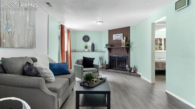 living room featuring a brick fireplace, wood-type flooring, and a textured ceiling