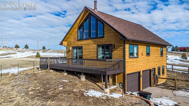 snow covered house with a garage and a wooden deck