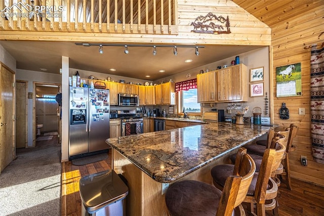 kitchen with dark wood-type flooring, a breakfast bar, sink, wood walls, and appliances with stainless steel finishes