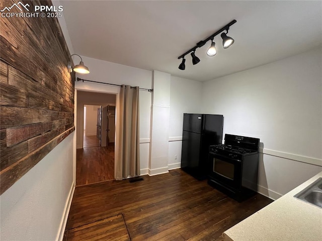 kitchen featuring sink, rail lighting, wooden walls, dark hardwood / wood-style floors, and black appliances