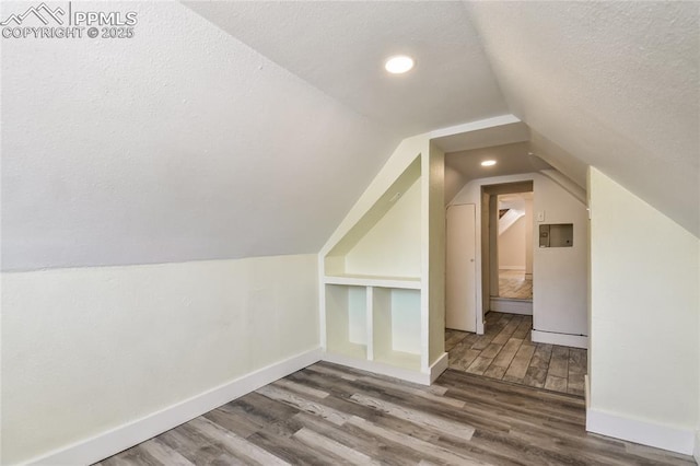 additional living space with hardwood / wood-style flooring, vaulted ceiling, built in features, and a textured ceiling