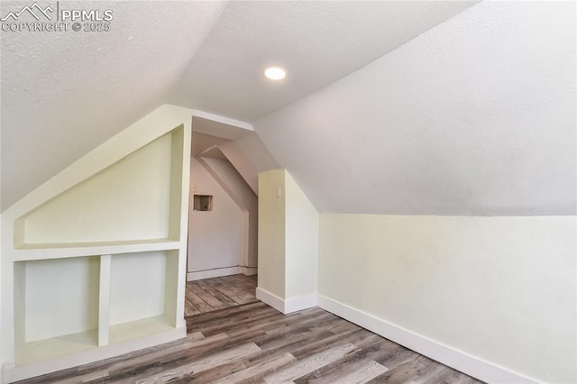 additional living space with lofted ceiling, hardwood / wood-style floors, built in features, and a textured ceiling