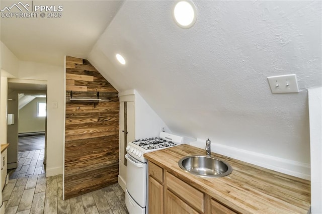 kitchen with sink, gas range gas stove, wood walls, a textured ceiling, and baseboard heating