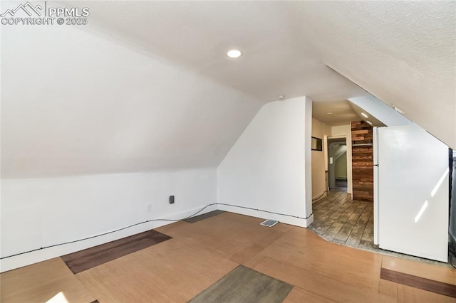 bonus room featuring lofted ceiling, light hardwood / wood-style floors, and a textured ceiling