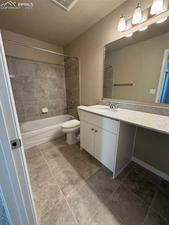 full bathroom featuring vanity, tiled shower / bath combo, a textured ceiling, and toilet