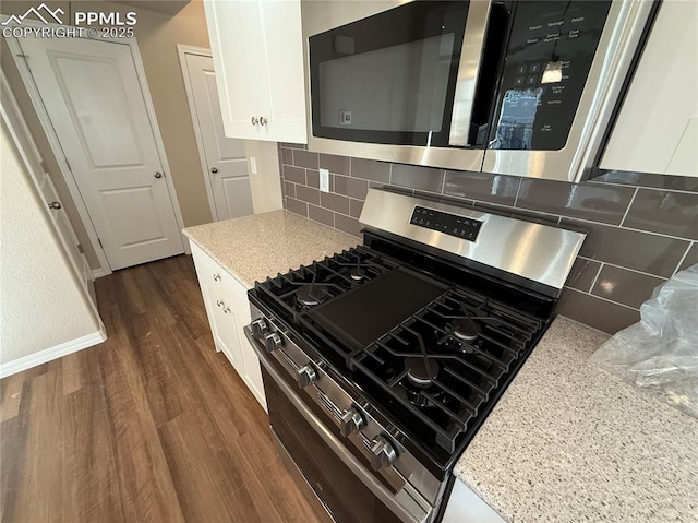 kitchen with appliances with stainless steel finishes, white cabinetry, backsplash, dark hardwood / wood-style floors, and light stone counters