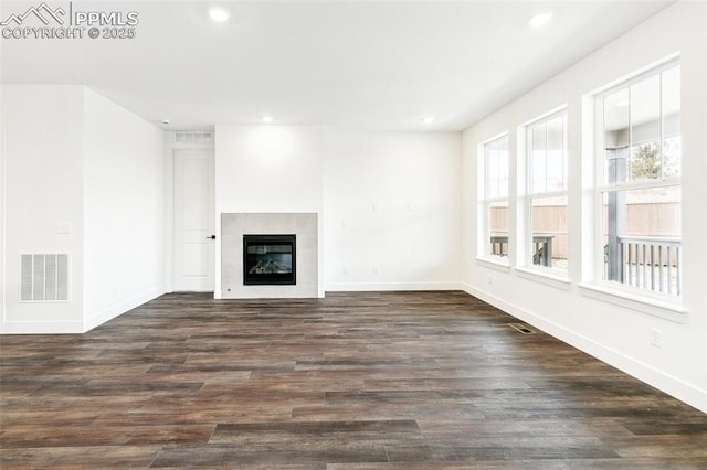 unfurnished living room featuring a tiled fireplace and dark hardwood / wood-style floors