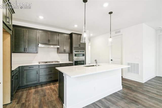 kitchen featuring sink, a center island with sink, appliances with stainless steel finishes, dark hardwood / wood-style flooring, and pendant lighting