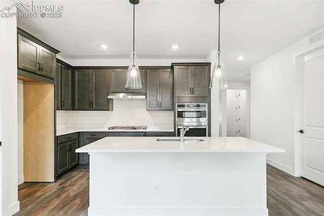 kitchen featuring stainless steel appliances, a kitchen island with sink, sink, and decorative light fixtures