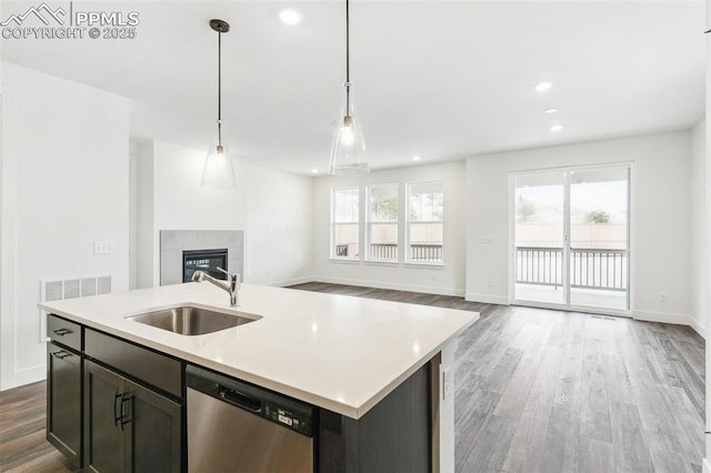 kitchen featuring sink, decorative light fixtures, a center island with sink, stainless steel dishwasher, and a fireplace