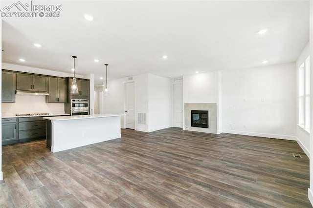 kitchen featuring double oven, hanging light fixtures, black electric stovetop, a kitchen island, and a tiled fireplace