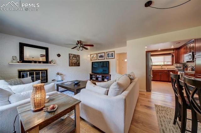 living room with ceiling fan, a brick fireplace, and light hardwood / wood-style floors