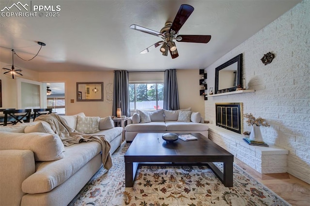 living room featuring a fireplace, ceiling fan, and light wood-type flooring