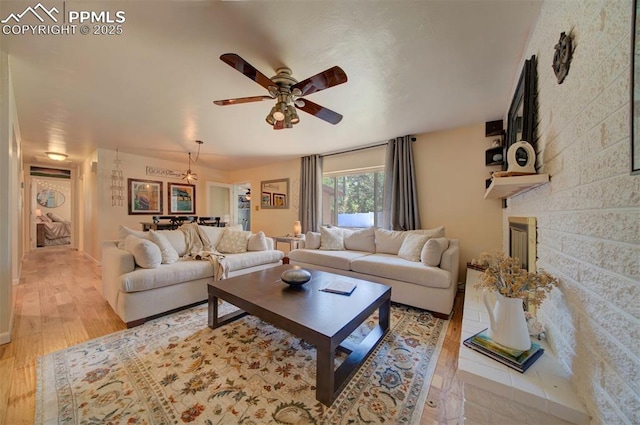 living room featuring a large fireplace, ceiling fan, and light wood-type flooring