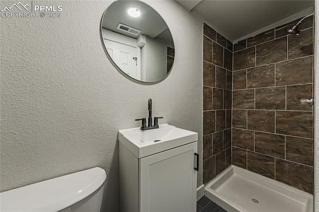 bathroom featuring a tile shower, vanity, and toilet