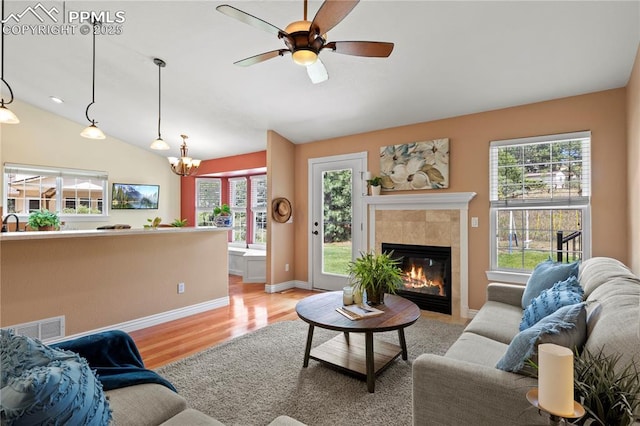 living room with light hardwood / wood-style flooring, ceiling fan with notable chandelier, a fireplace, and lofted ceiling