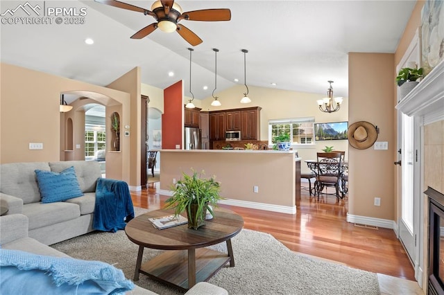 living room featuring a tiled fireplace, lofted ceiling, ceiling fan with notable chandelier, and light wood-type flooring