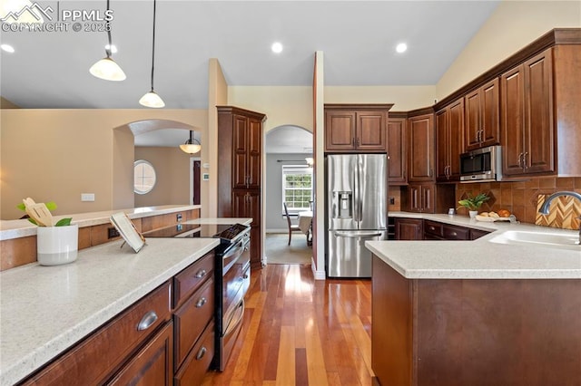 kitchen with appliances with stainless steel finishes, wood-type flooring, sink, decorative backsplash, and hanging light fixtures