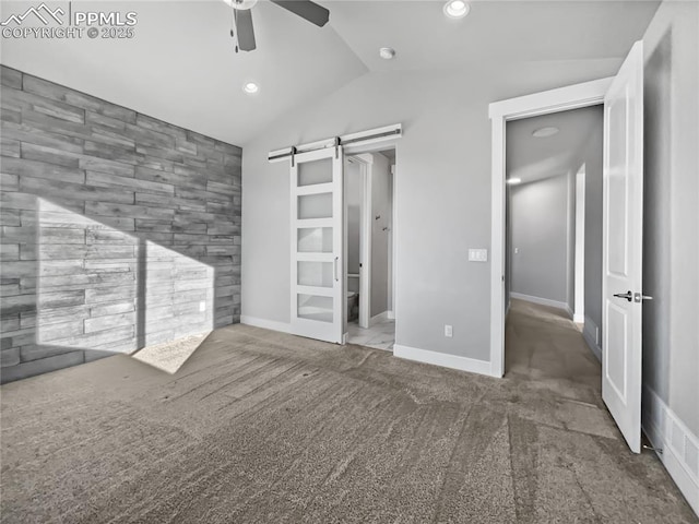 unfurnished bedroom featuring ceiling fan, a barn door, vaulted ceiling, and carpet