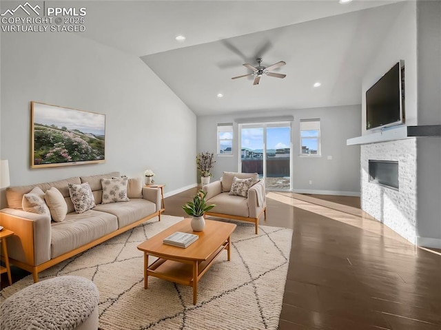 living room featuring a stone fireplace, vaulted ceiling, ceiling fan, and light wood-type flooring