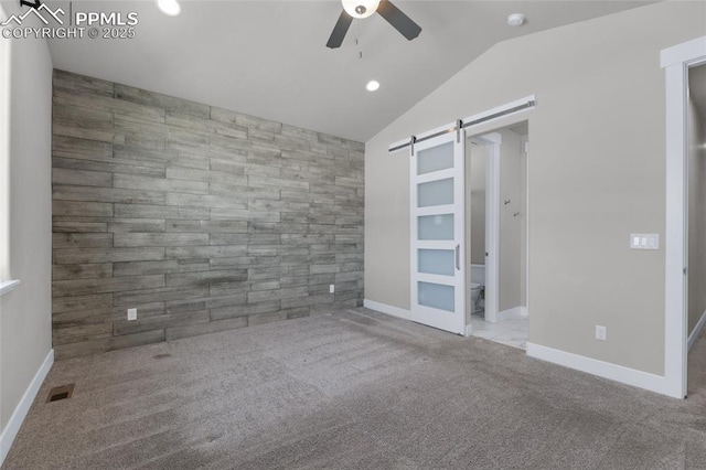 spare room with wooden walls, a barn door, and light carpet