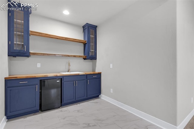 kitchen featuring fridge, sink, butcher block counters, and blue cabinetry