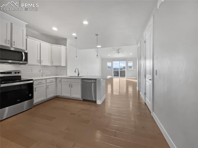 kitchen featuring sink, decorative light fixtures, appliances with stainless steel finishes, kitchen peninsula, and white cabinets