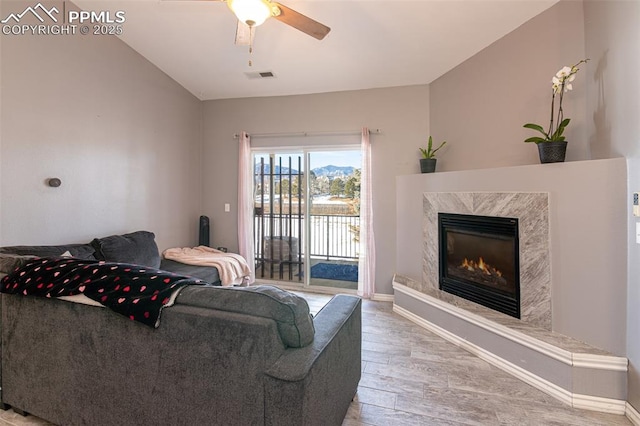 living room featuring hardwood / wood-style flooring, vaulted ceiling, a premium fireplace, and ceiling fan