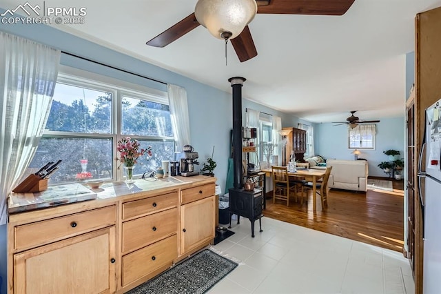 kitchen featuring ceiling fan, refrigerator, light brown cabinets, and a wood stove