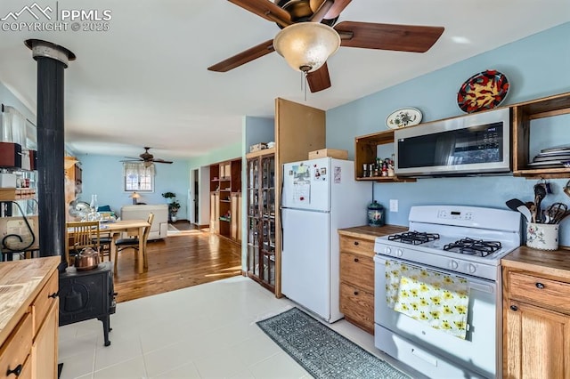 kitchen with butcher block countertops, a wood stove, ceiling fan, and white appliances