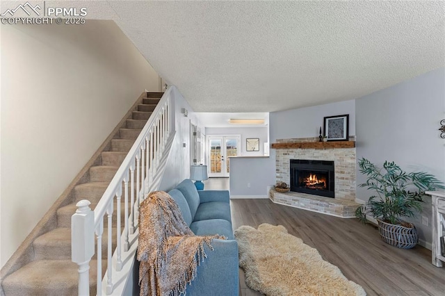 living room with a wall mounted air conditioner, wood-type flooring, a brick fireplace, and a textured ceiling